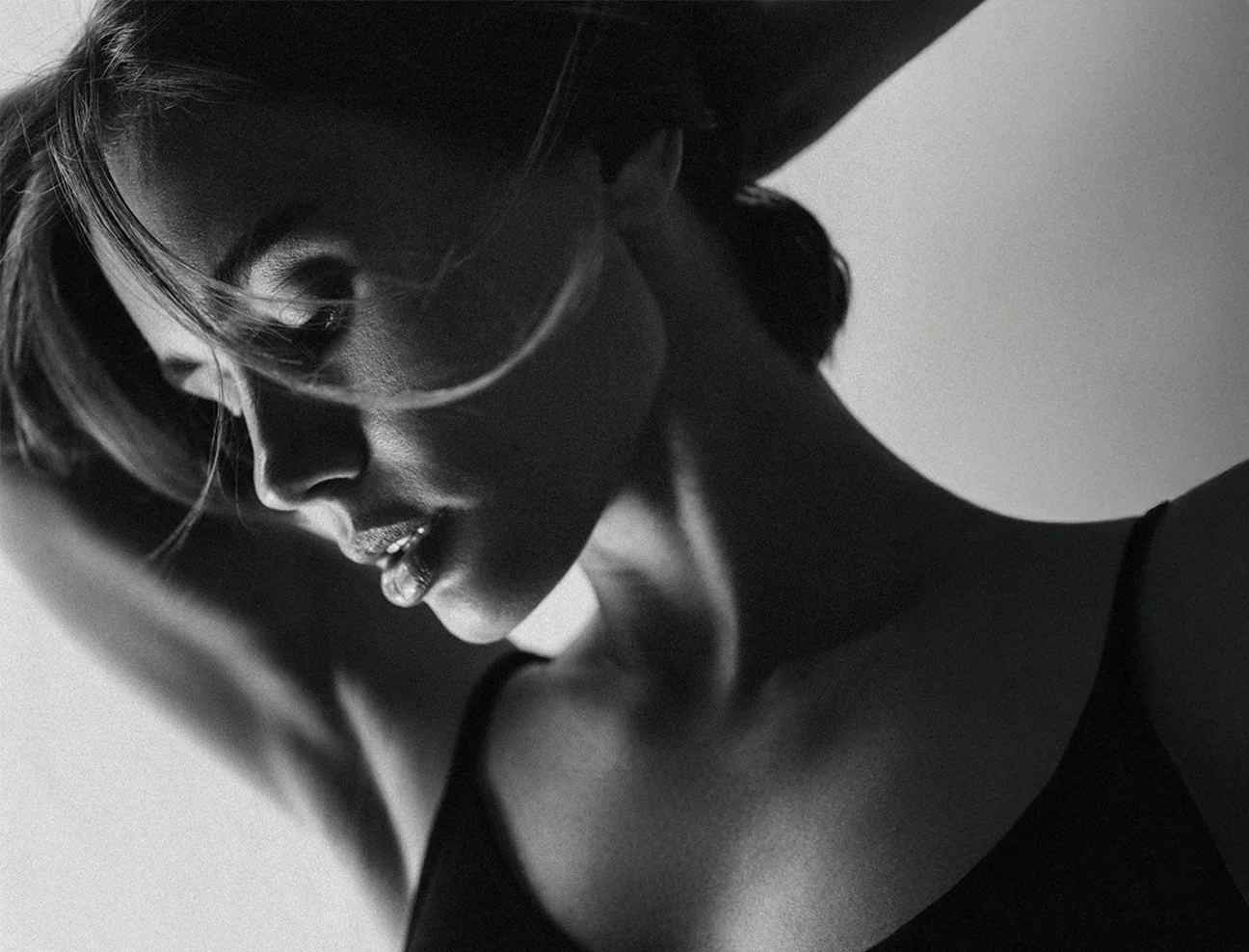 A grainy, high-contrast black-and-white shot of a woman in profile, looking down with her hair blowing softly across her face.