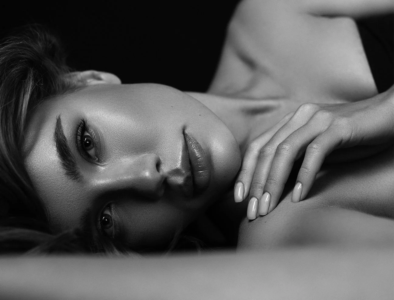 A top-down view of a woman lying down with her hair fanned out. She is looking into the camera with a calm, luminous expression.