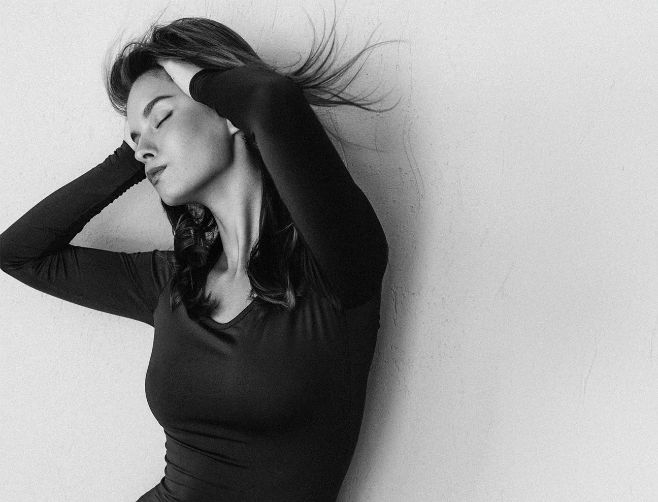 A woman in a black long-sleeved top leans back with her eyes closed and hands in her hair. The image captures a sense of energy and revitalization.